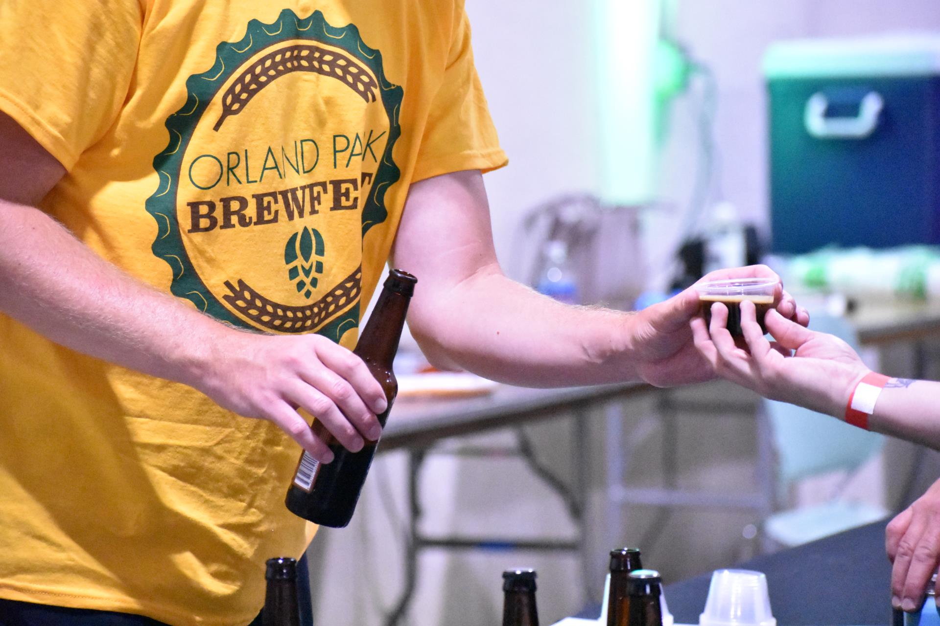 A man wearing a yellow tshirt with Brewfest logo offers a sample of dark beer to an attendee at the 2021 Brewfest